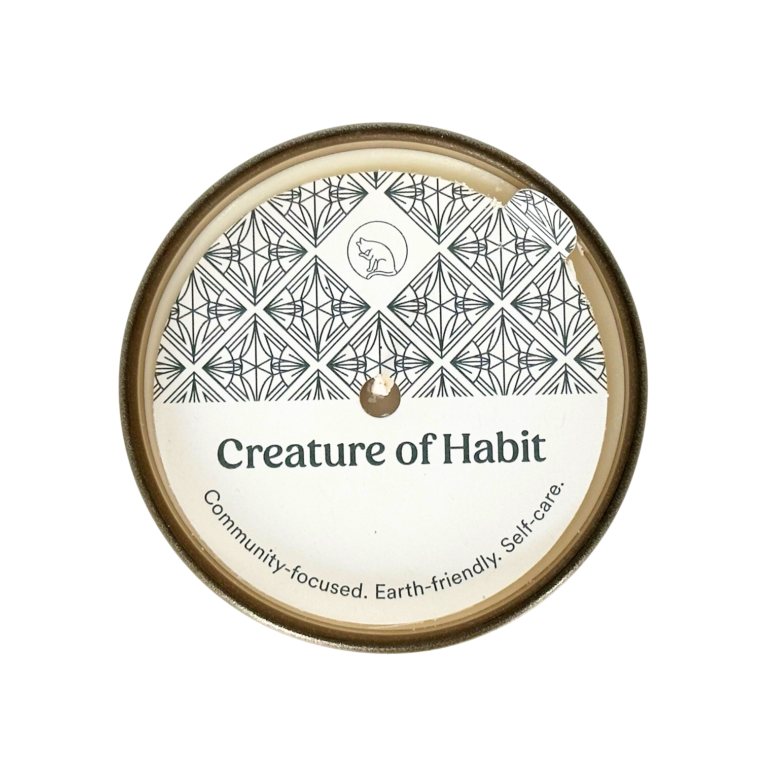 A top-down view of a candle is shown with a dust cover. The dust cover features the Creature of Habit logo, a silhouette of a cat, within a repeating art deco pattern. The company name Creature of Habit is featured along with the tagline, "Community-focused. Earth-friendly. Self-care.”