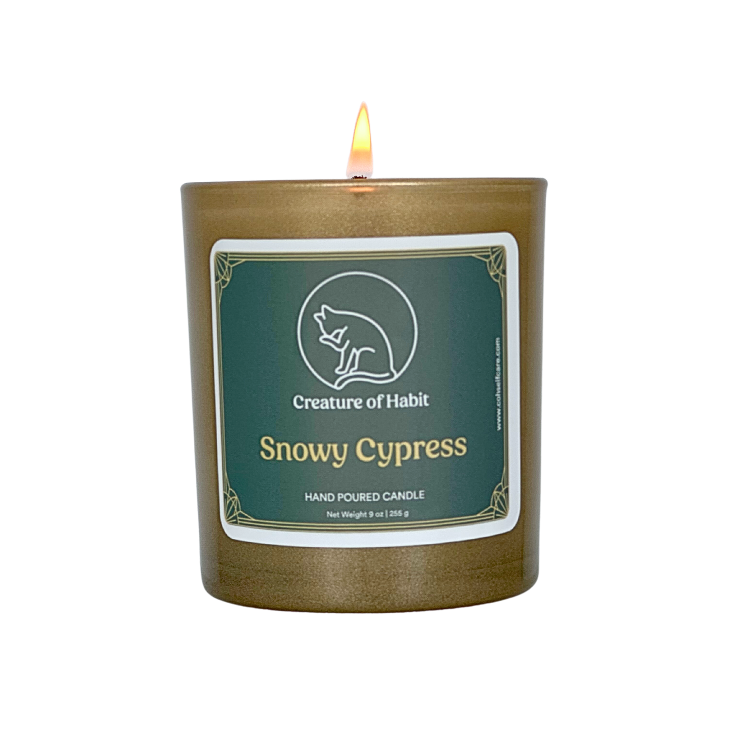 A lit soy candle within a golden vessel is against a white background. The label is greyish cyan featuring the logo of a white cat silhouette, the name of the company Creature of Habit, and the scent name Snowy Cypress.